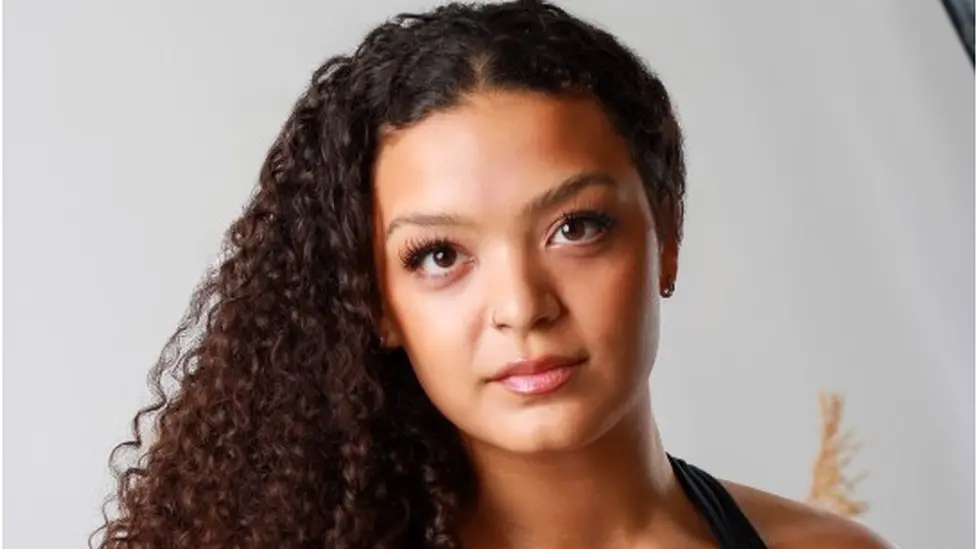 Portrait of Tynisha Abdy, who is calling for businesses and schools to train staff to better understand autism. She has long, curly hair and is looking directly at the camera with a calm expression.