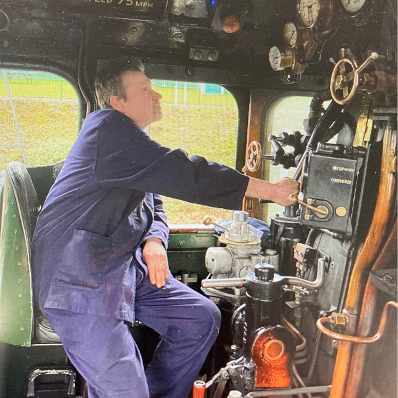A picture of Peter Dickson in navy overalls driving a train