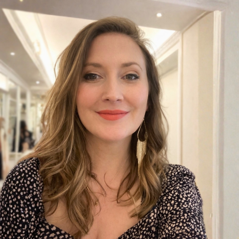 Richmal, smiling at the camera with red lipstick and gold statement earrings